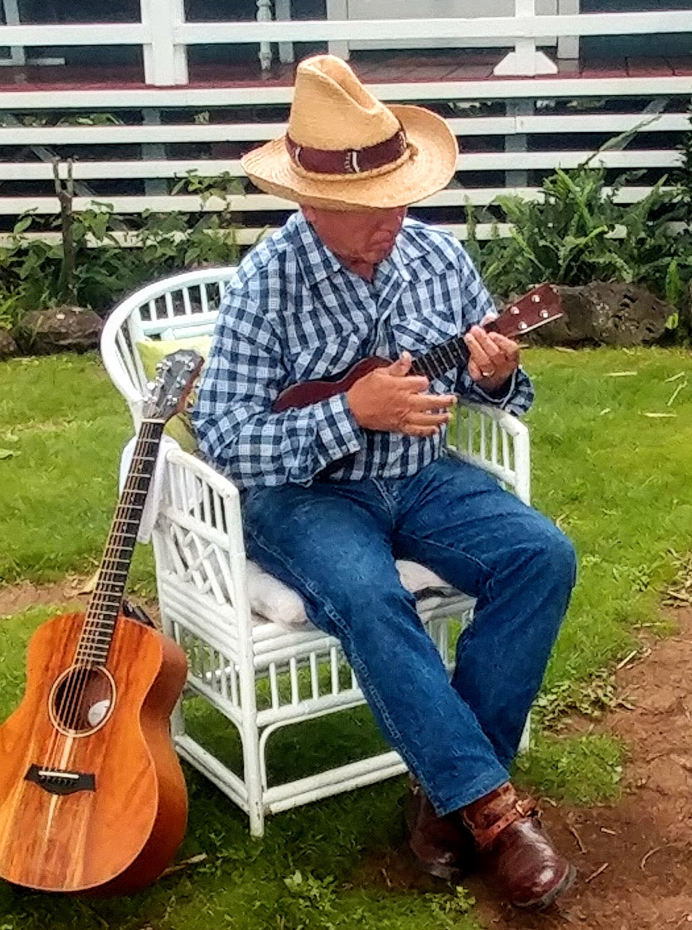 Danny Akaka in a cowboy hat and palaka shirt, sitting with a guitar